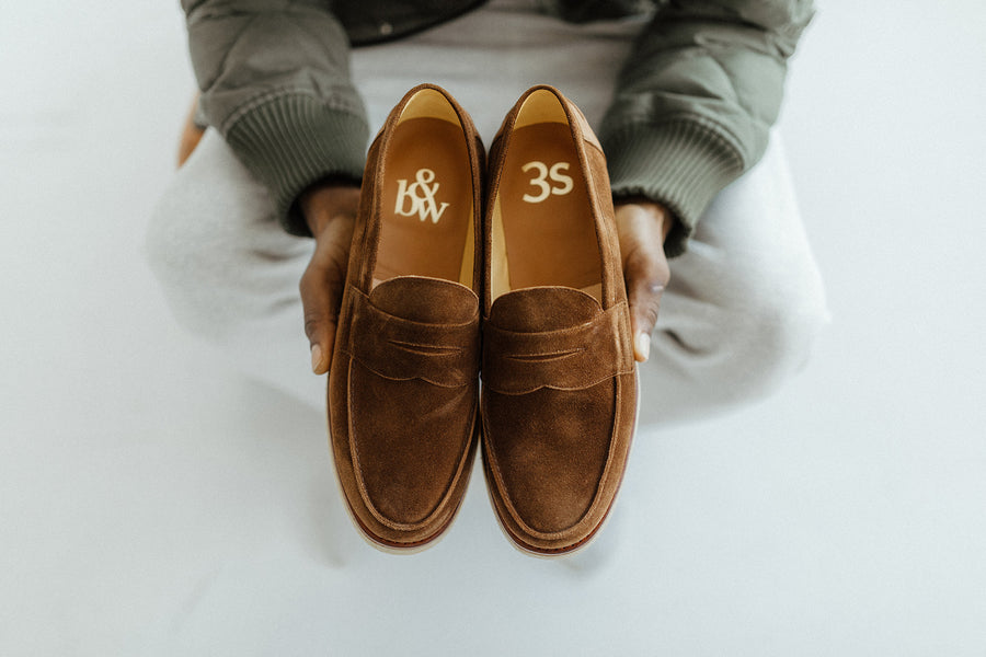 Hands hold a pair of loafers with gold foil brand stampings on the inside of both B&W and 3s.