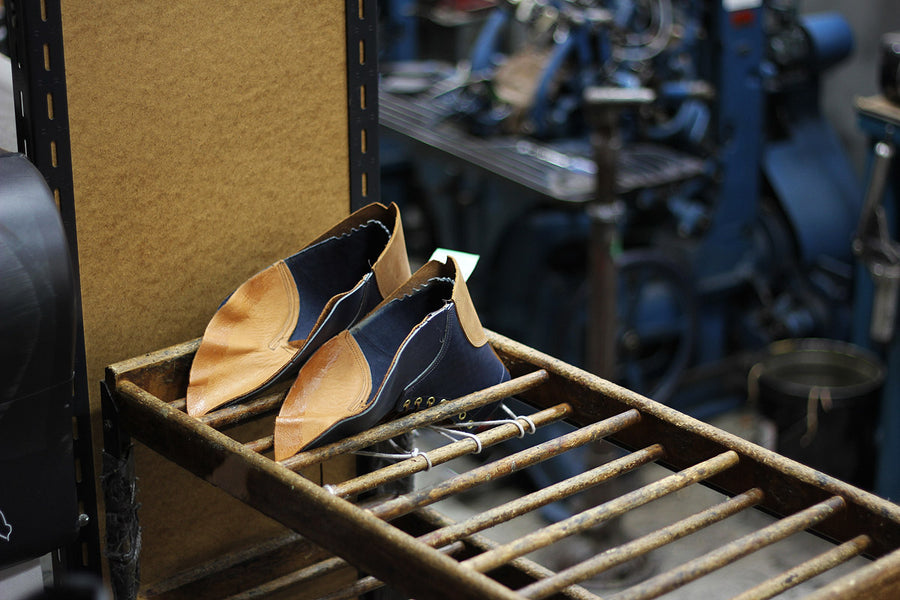 Partially sewn boot uppers sit on wooden racks awaiting lasting.