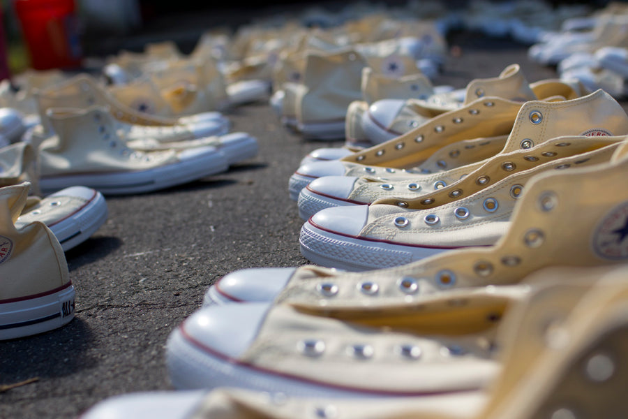 A sea of white Connverse sneakers sit on the pavement.