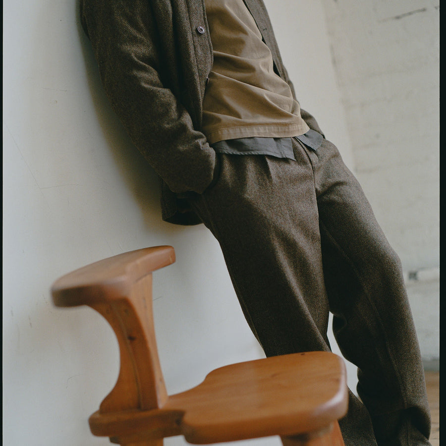 A man in earth toned clothing stands next to a chair.