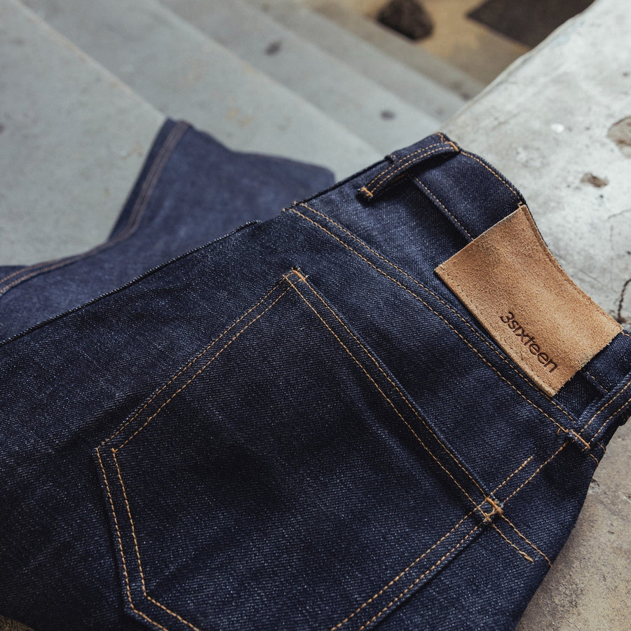 A pair of raw denim blue jeans folded on the floor.