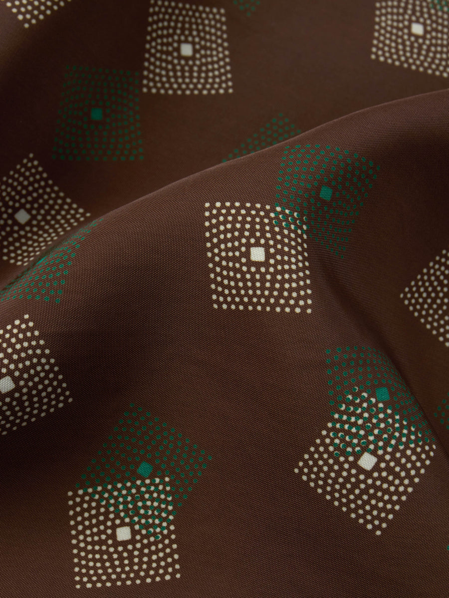 A close-up of a brown fabric with a repeating geometric pattern of dotted squares in cream and green.