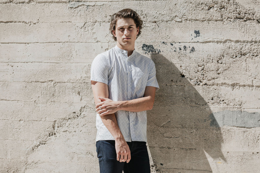 Man wears band collar shirt in front of wall.