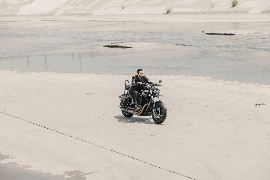 Model wearing leather jacket while riding on a motorcycle near LA river.
