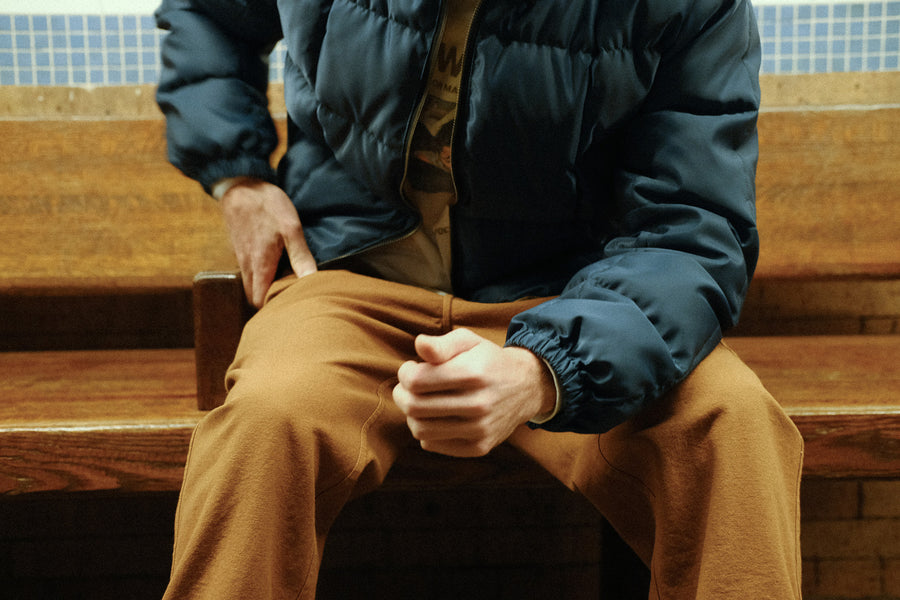 A photo of a blue down jacket worn by someone sitting on a wooden bench. 