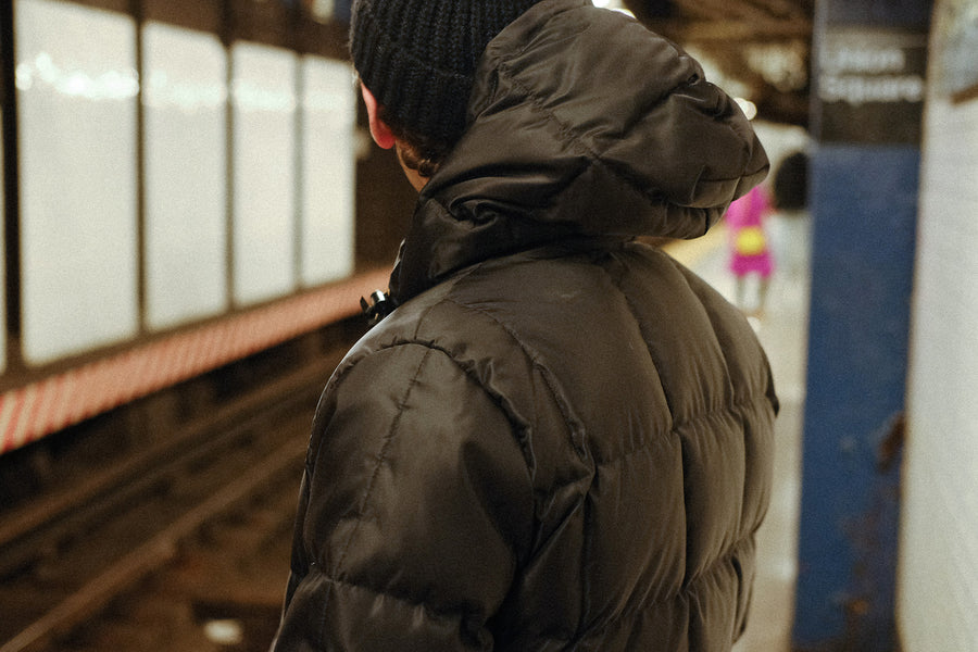 A man in a black puffer jacket stands on a subway platform.