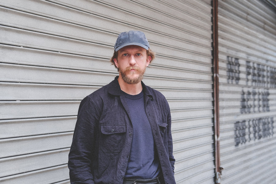 A man wears a worn-in baseball cap against a grey security gate.